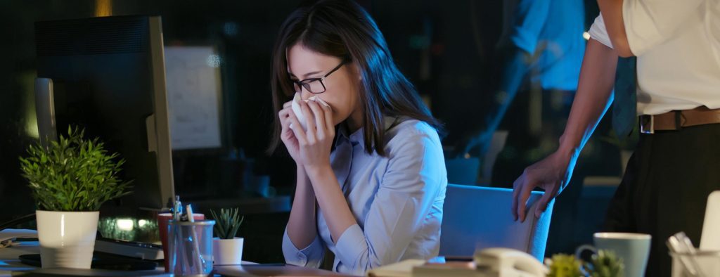 person blowing their nose at desk